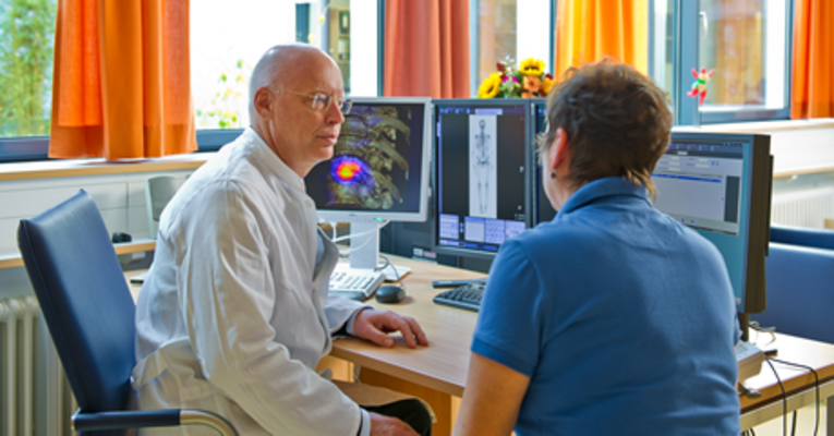 Prof. Dr. Torsten Kuwert im Gespräch mit einer Patientin vor drei Monitoren mit SPECT/CT-Aufnahmen.